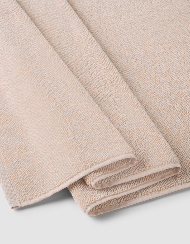 A Loop Terry Bath Mat by Cozy Earth, in light beige with a soft, textured surface, is neatly folded and stacked on a white background.