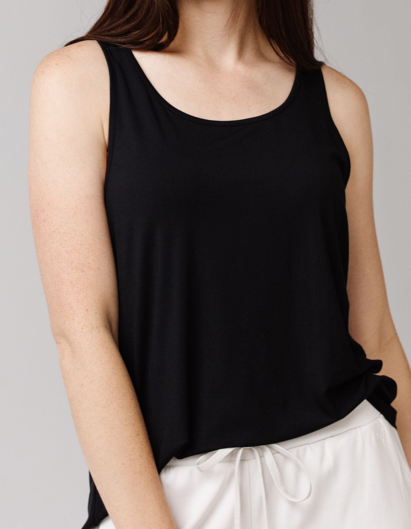 A woman wears the Cozy Earth Women's Bamboo Stretch-Knit Lounge Tank in black. She stands against a plain background, with her loose brown hair over her shoulders and face partially out of frame.
