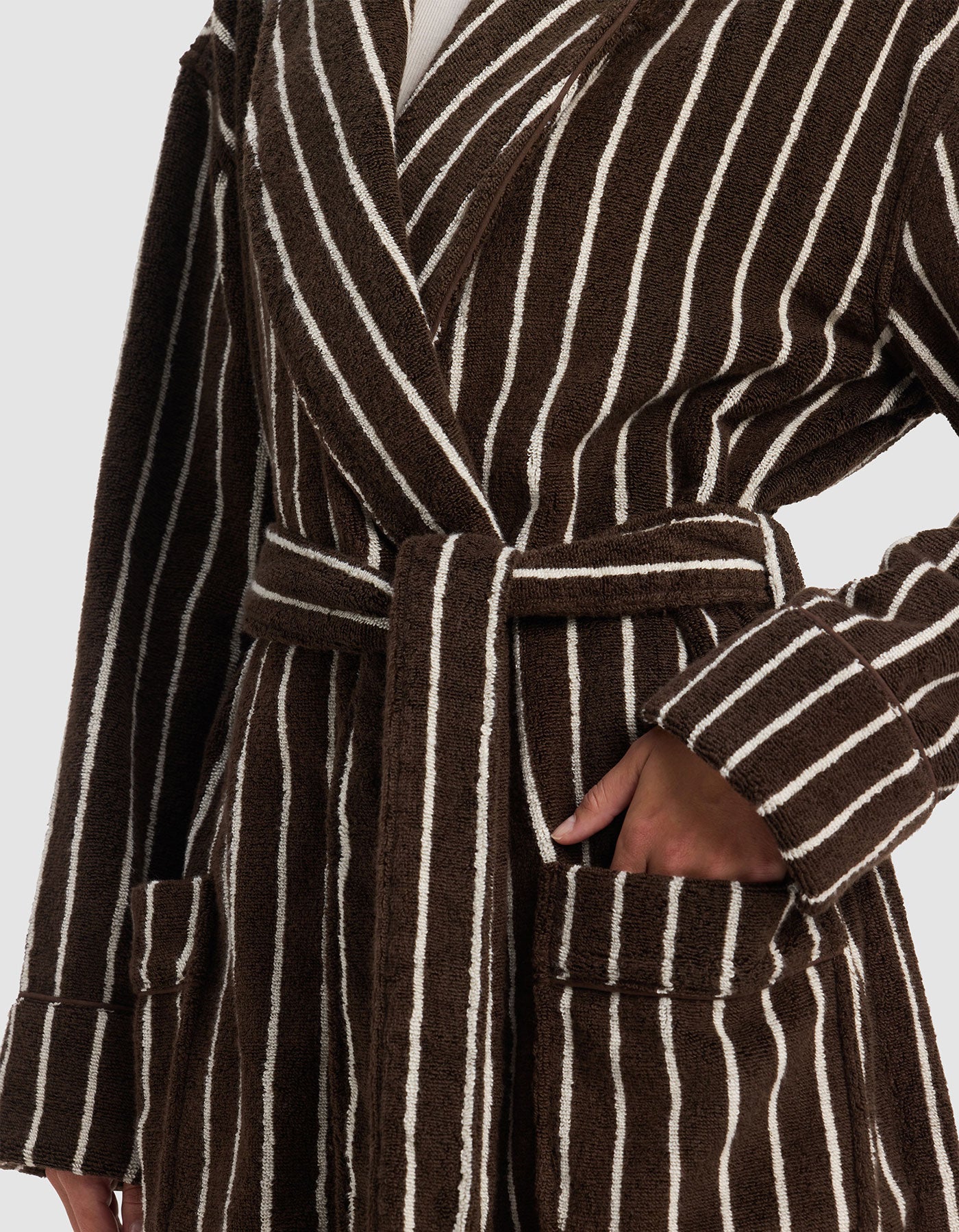 A person wearing the Cozy Earth Striped Luxe Bath Robe, featuring brown and white vertical stripes, a waist belt, and their left hand in the pocket.|Color:Espresso Coconut Stripe