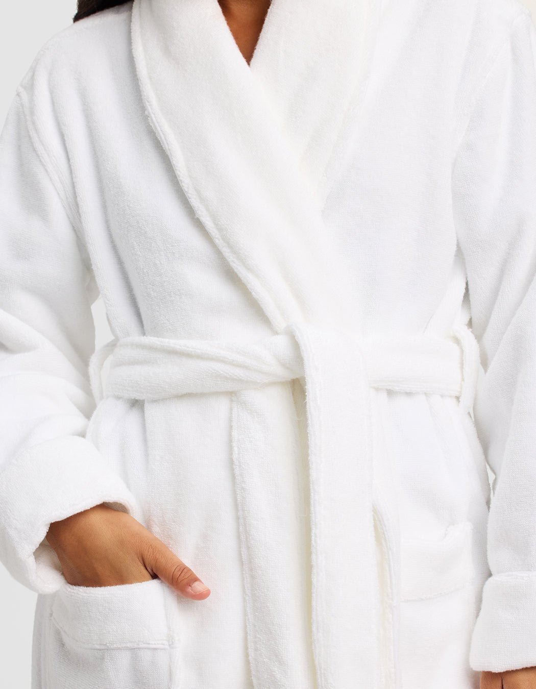 A person models the Luxe Bath Robe by Cozy Earth in plush white, belted at the waist with one hand in a pocket. The cropped image shows only the body, not the face.