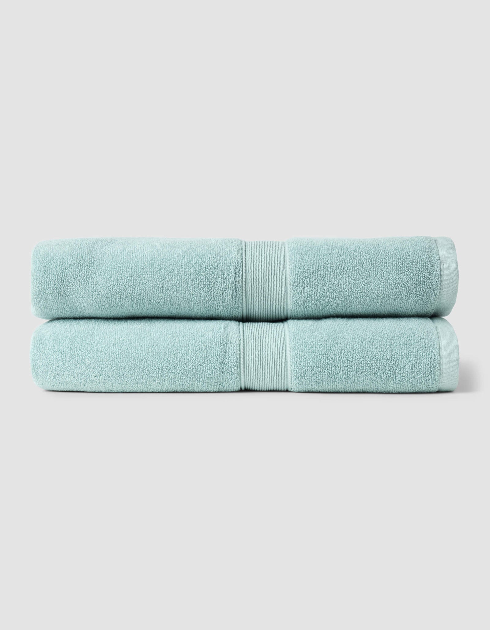 Two neatly folded light blue towels from the Cozy Earth Complete Luxe Bath Bundle are stacked against a plain, light gray background.