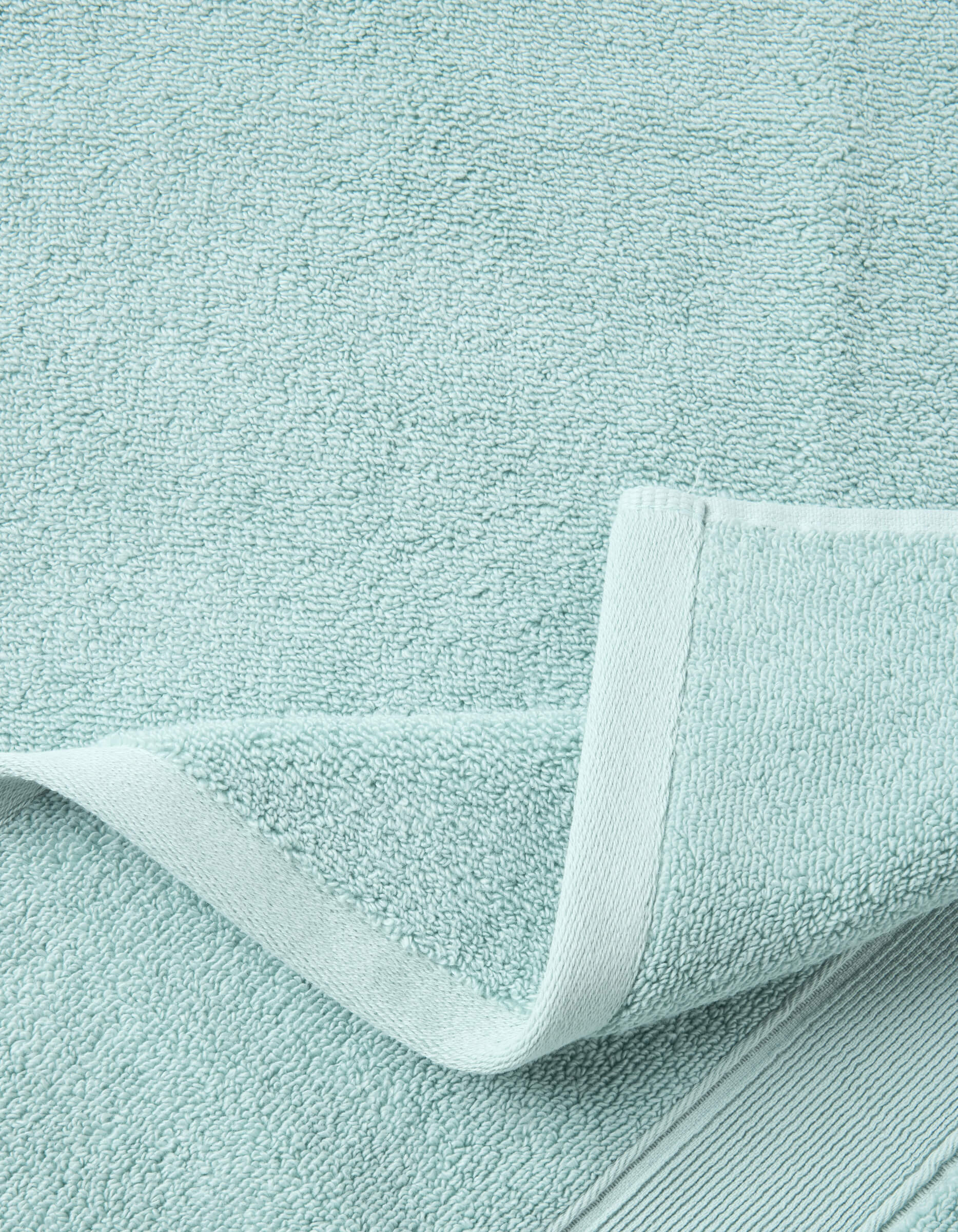 A close-up of the Luxe Bath Sheets by Cozy Earth in light blue highlights their textured, soft surface and neatly folded edge, showcasing the towel’s plush thickness and detailed hem.|Color:Tide