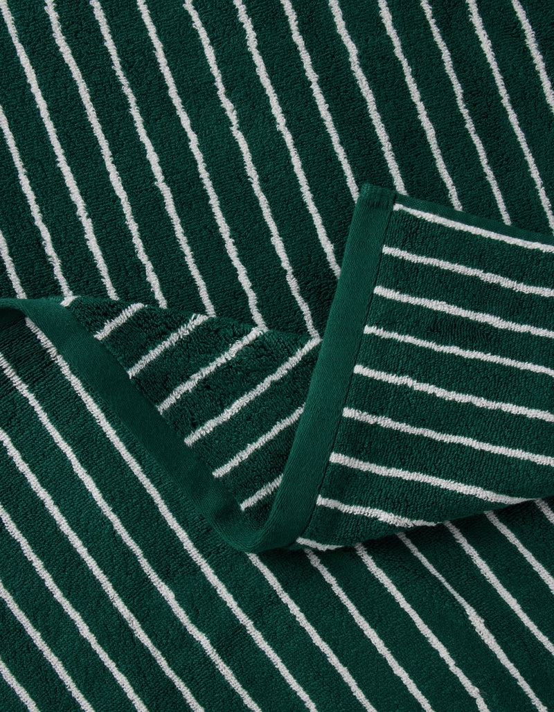A close-up of the Luxe Bath Towel Set by Cozy Earth, featuring dark green fabric with white horizontal stripes and a folded corner showing the pattern on both sides.