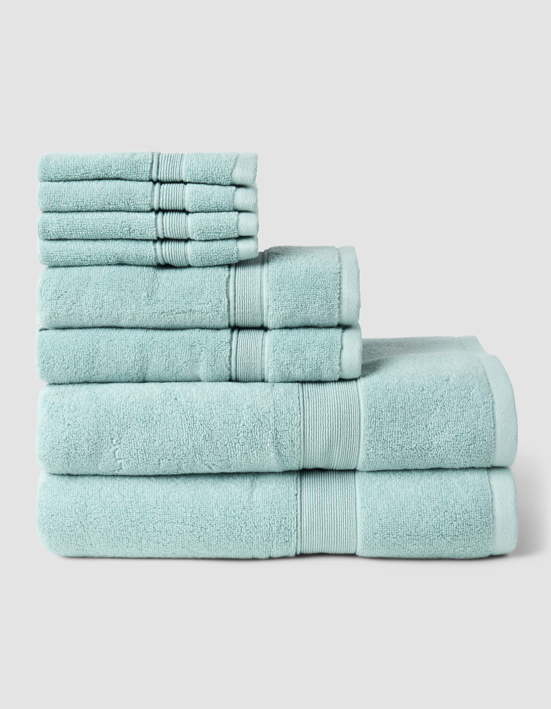 The Luxe Bath Towel Set by Cozy Earth is displayed in three neatly stacked tiers of light blue towels in different sizes, set against a plain light gray background.|Color:Tide
