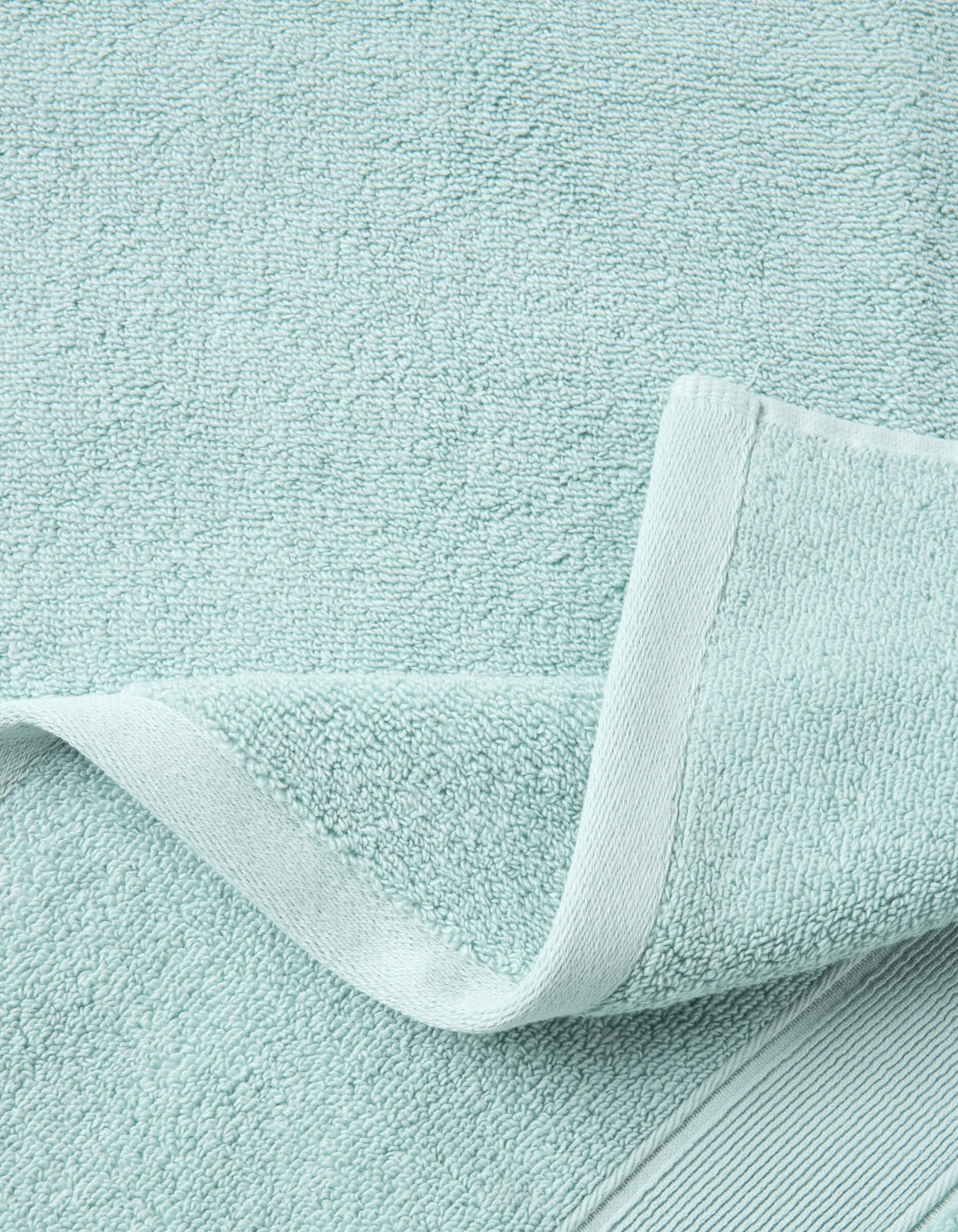 A close-up of the Luxe Bath Towel Set by Cozy Earth in light blue, featuring a woven border and folded corner that highlights the soft, absorbent fabric's texture.