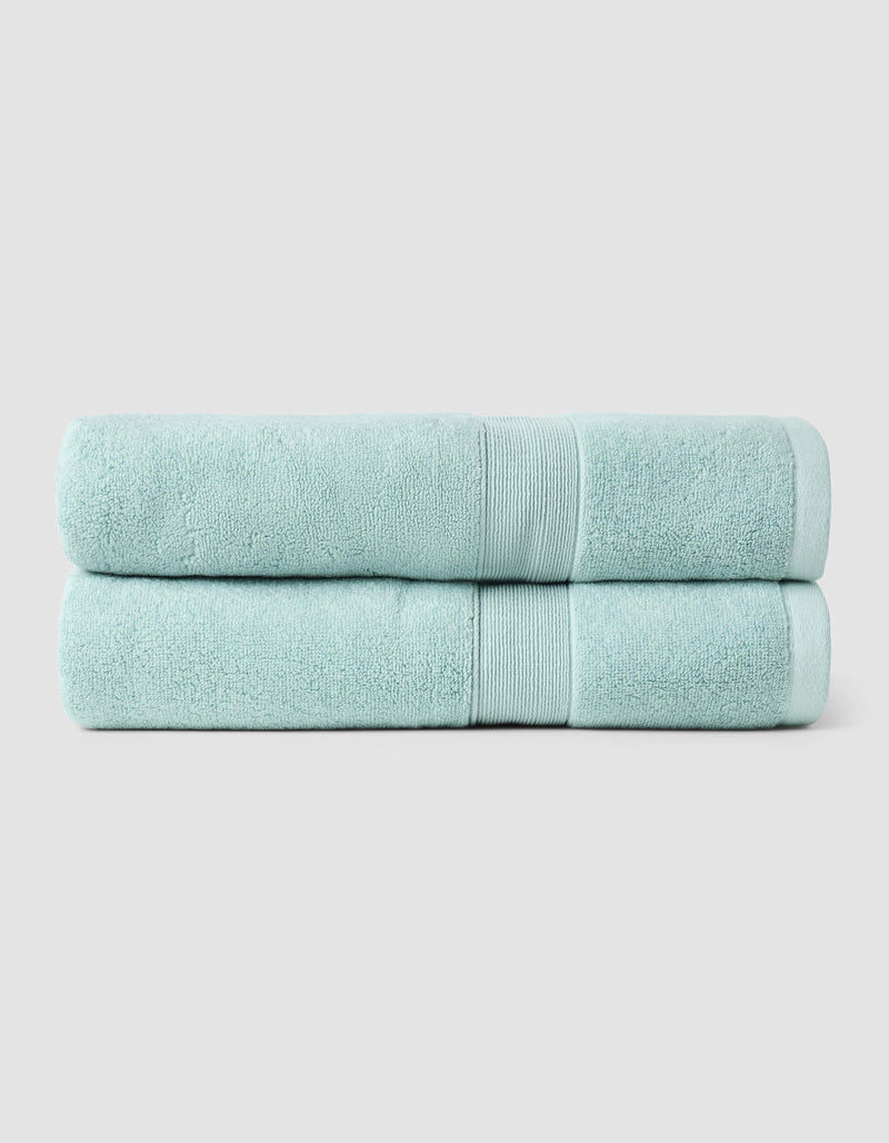 Two Luxe Bath Towels by Cozy Earth, neatly folded and stacked, are displayed against a plain light gray background.