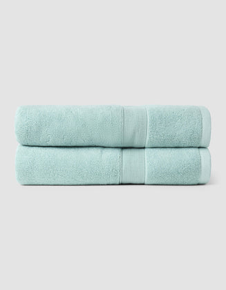 Two Luxe Bath Towels by Cozy Earth, neatly folded and stacked, are displayed against a plain light gray background.|Color:Tide