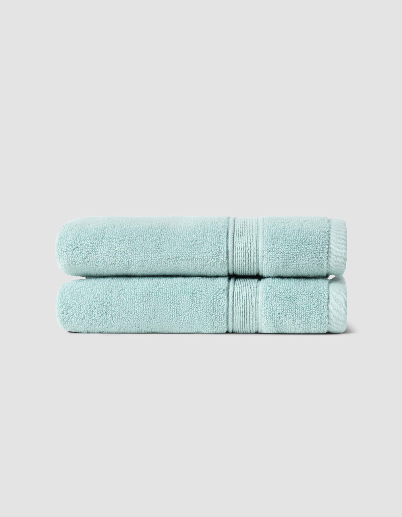 Two neatly folded Luxe Hand Towels by Cozy Earth, in light blue, are stacked atop each other against a plain light gray background.|Color:Tide