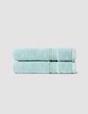 Two neatly folded Luxe Hand Towels by Cozy Earth, in light blue, are stacked atop each other against a plain light gray background.|Color:Tide