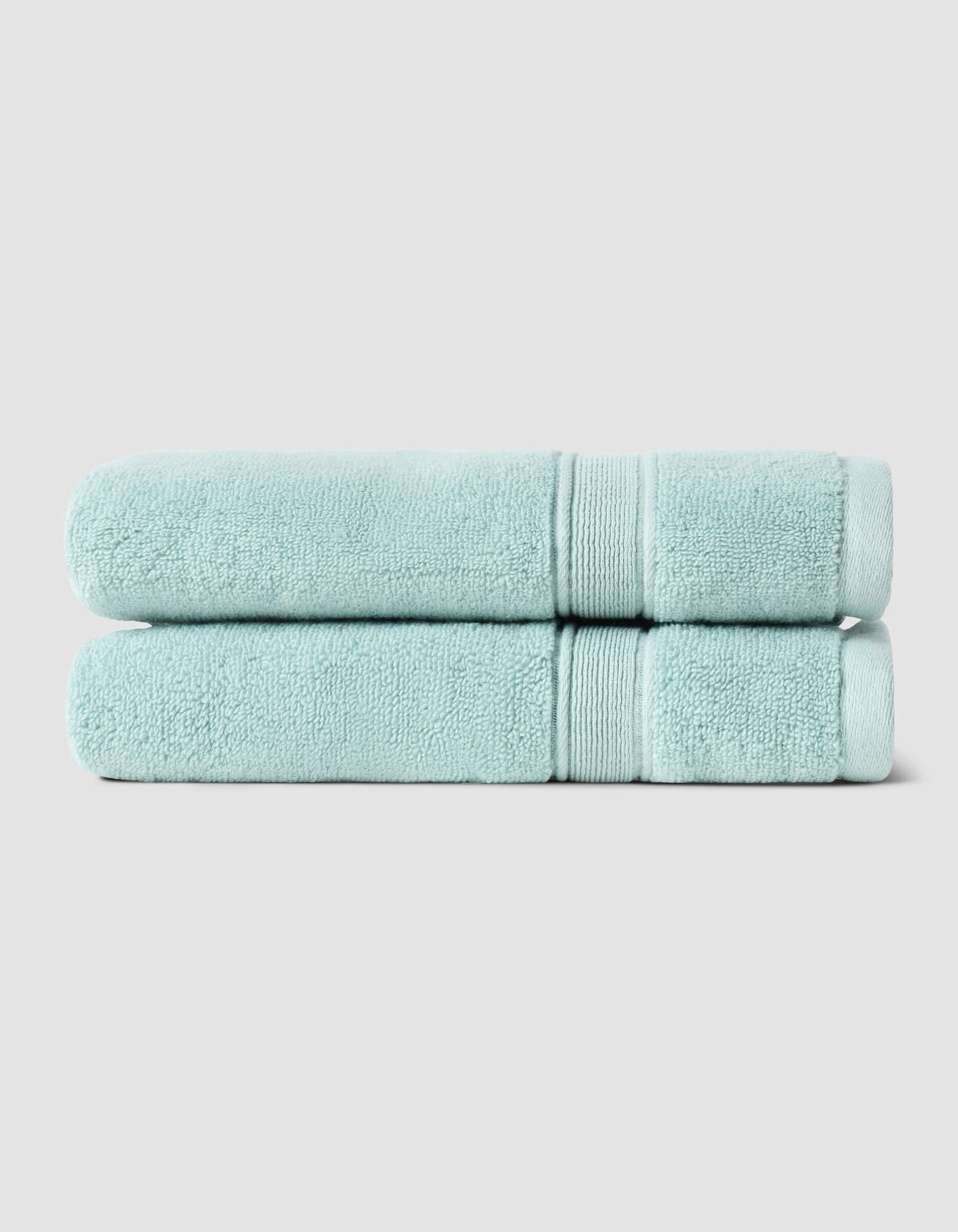 Two neatly folded Luxe Hand Towels by Cozy Earth, in light blue, are stacked atop each other against a plain light gray background.