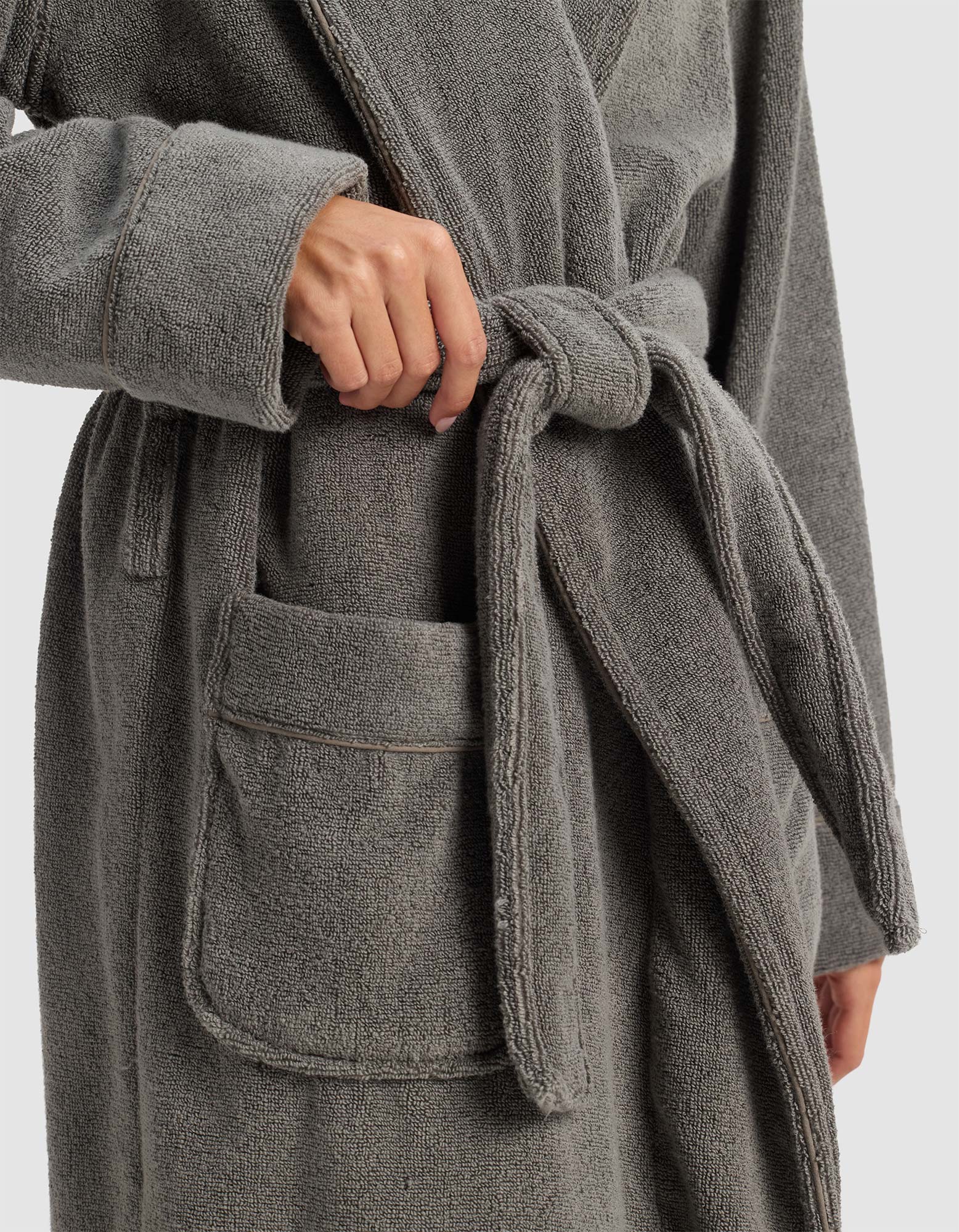 A person in the Cozy Earth Luxe Bath Robe ties the waist belt; one hand loops the belt, and the plush robe features a spacious front pocket.