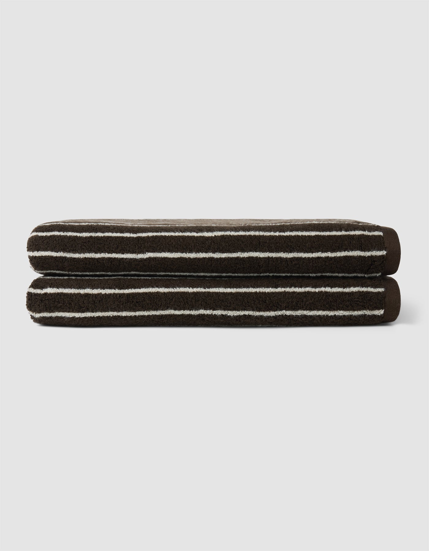 Two neatly folded Cozy Earth Complete Striped Luxe Bath Bundle towels, featuring dark brown color with thin white stripes, are stacked against a plain light gray background.