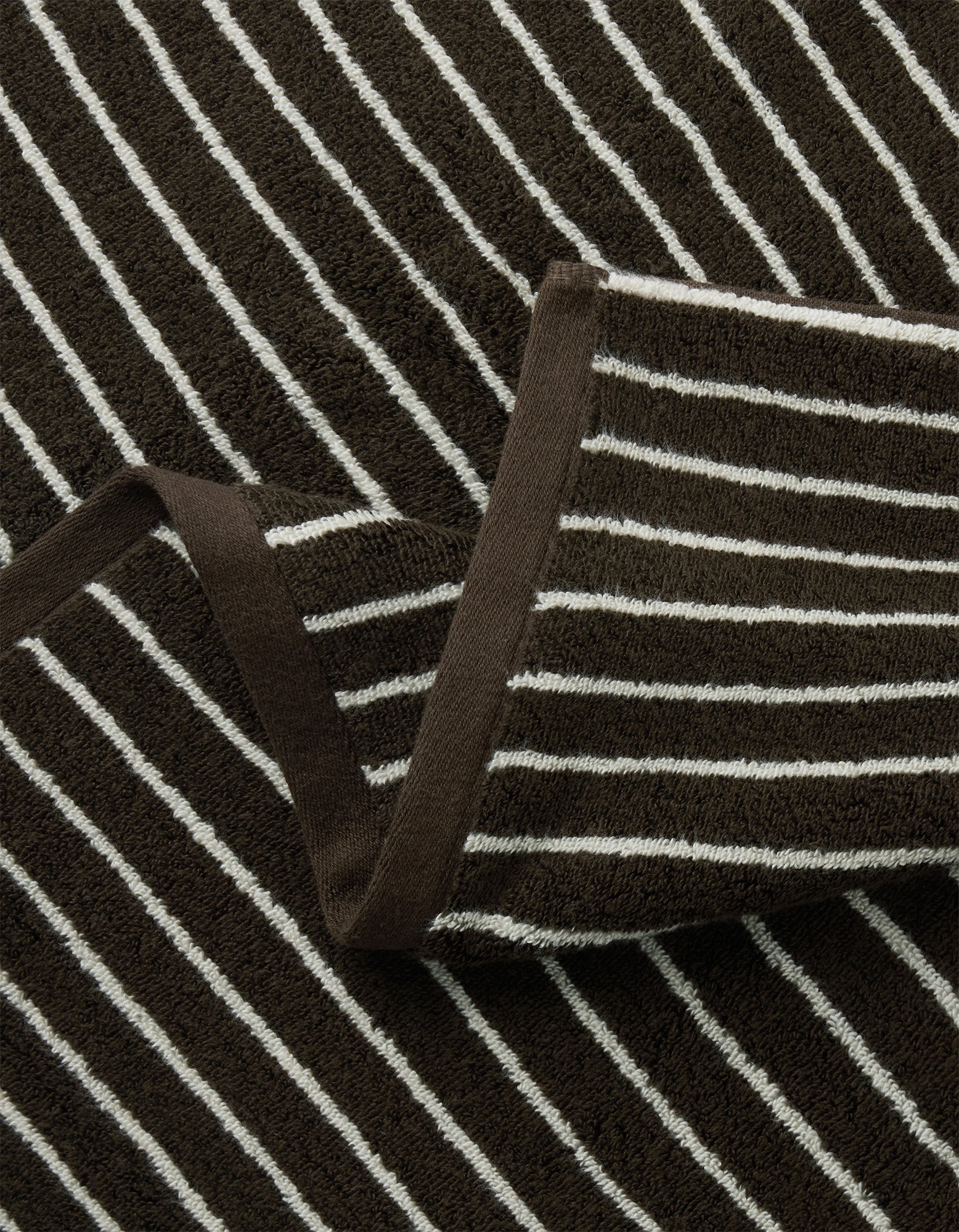Close-up of Cozy Earth's Striped Luxe Bath Sheets in brown with white horizontal stripes and a brown trim, shown layered on matching striped material.