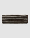 The Complete Striped Luxe Bath Bundle by Cozy Earth features two dark brown towels with thin, irregular white stripes, neatly rolled and stacked on a light gray background.|Color:Espresso Coconut Stripe