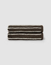 Two neatly rolled Striped Luxe Bath Towels by Cozy Earth, featuring dark brown with white horizontal stripes, are stacked atop each other against a plain light background.|Color:Espresso Coconut Stripe