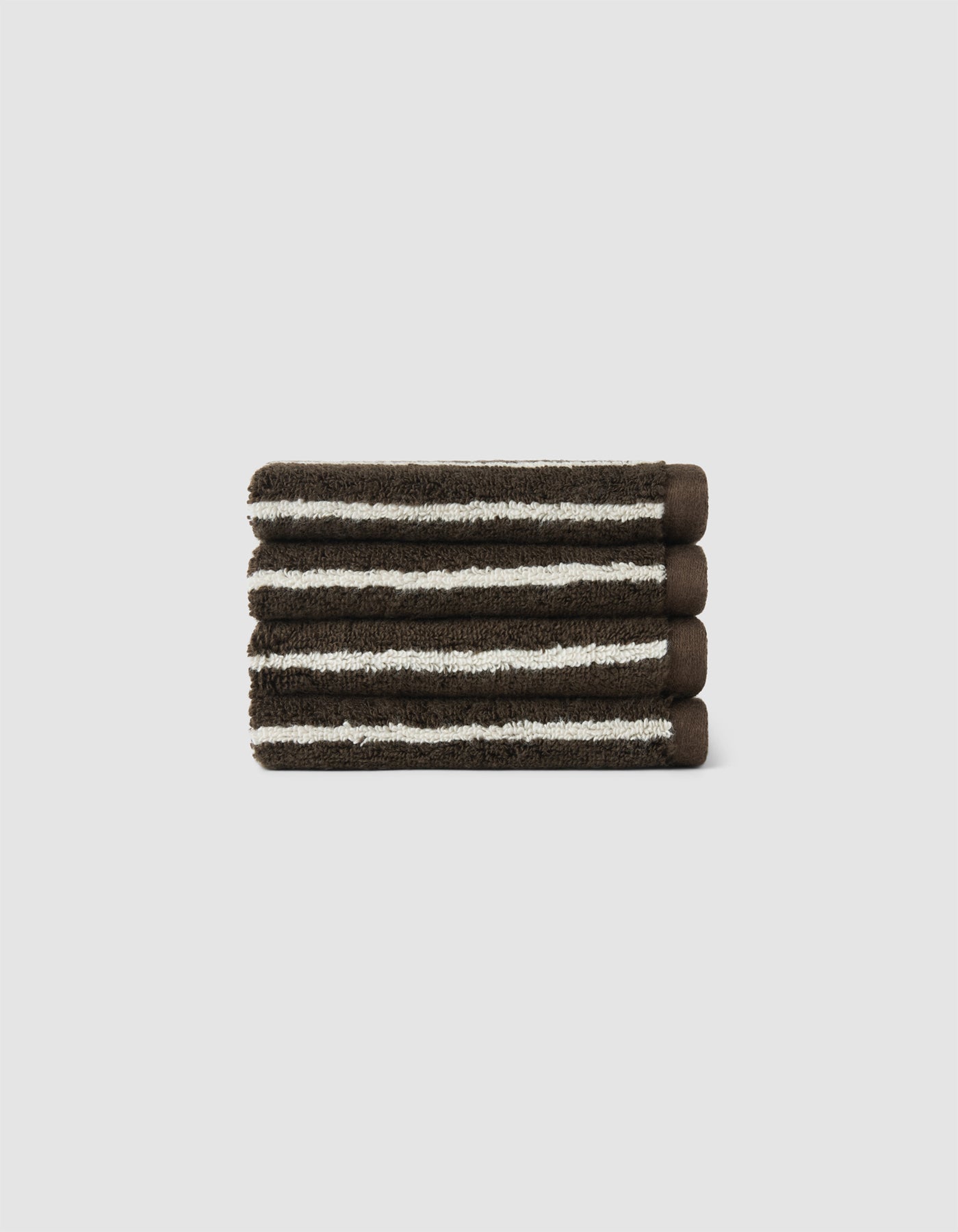 The Cozy Earth Complete Striped Luxe Bath Bundle features three neatly folded, dark brown towels with white stripes stacked together against a plain light gray background.