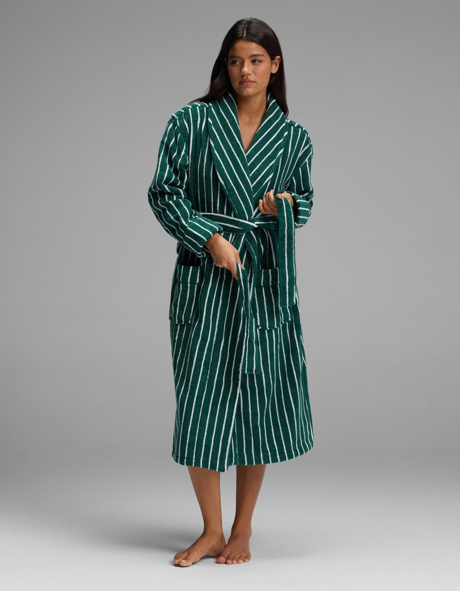 A woman stands barefoot against a plain gray background, wearing the Cozy Earth Luxe Bath Robe in green and white stripes and holding its waist tie.|Color:Uniform with Seashell Stripe