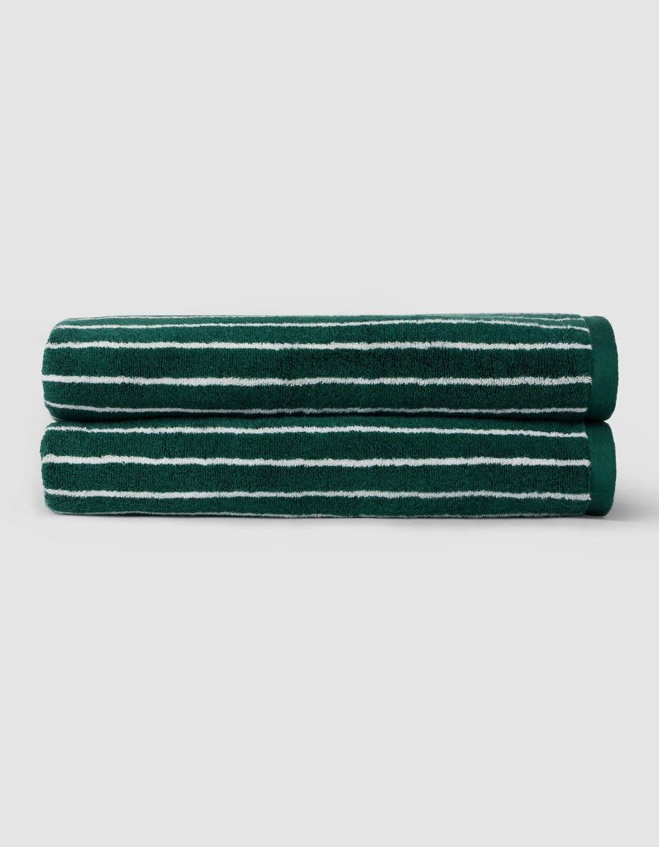 Two Luxe Bath Sheets by Cozy Earth in dark green with thin white stripes are neatly folded and stacked against a plain light gray background.|Color:Uniform with Seashell Stripe