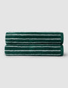 Two Luxe Bath Towels by Cozy Earth, dark green with white horizontal stripes, are neatly rolled and stacked on a light gray background.|Color:Uniform with Seashell Stripe
