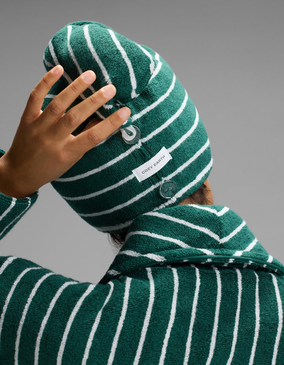 A person seen from behind adjusts their Luxe Hair Towel by Cozy Earth, featuring green and white stripes, labels, and two buttons.