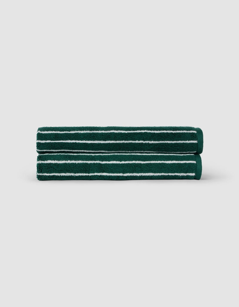 Two Luxe Hand Towels by Cozy Earth, dark green with white horizontal stripes, are neatly rolled and stacked against a plain light gray background.
