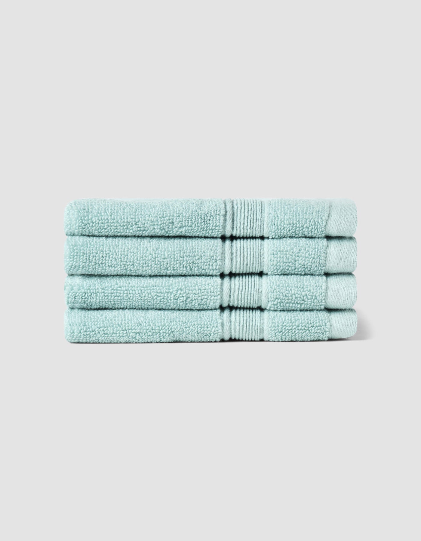 Four Luxe Washcloths by Cozy Earth, neatly folded in light blue, are stacked uniformly against a plain light gray background.