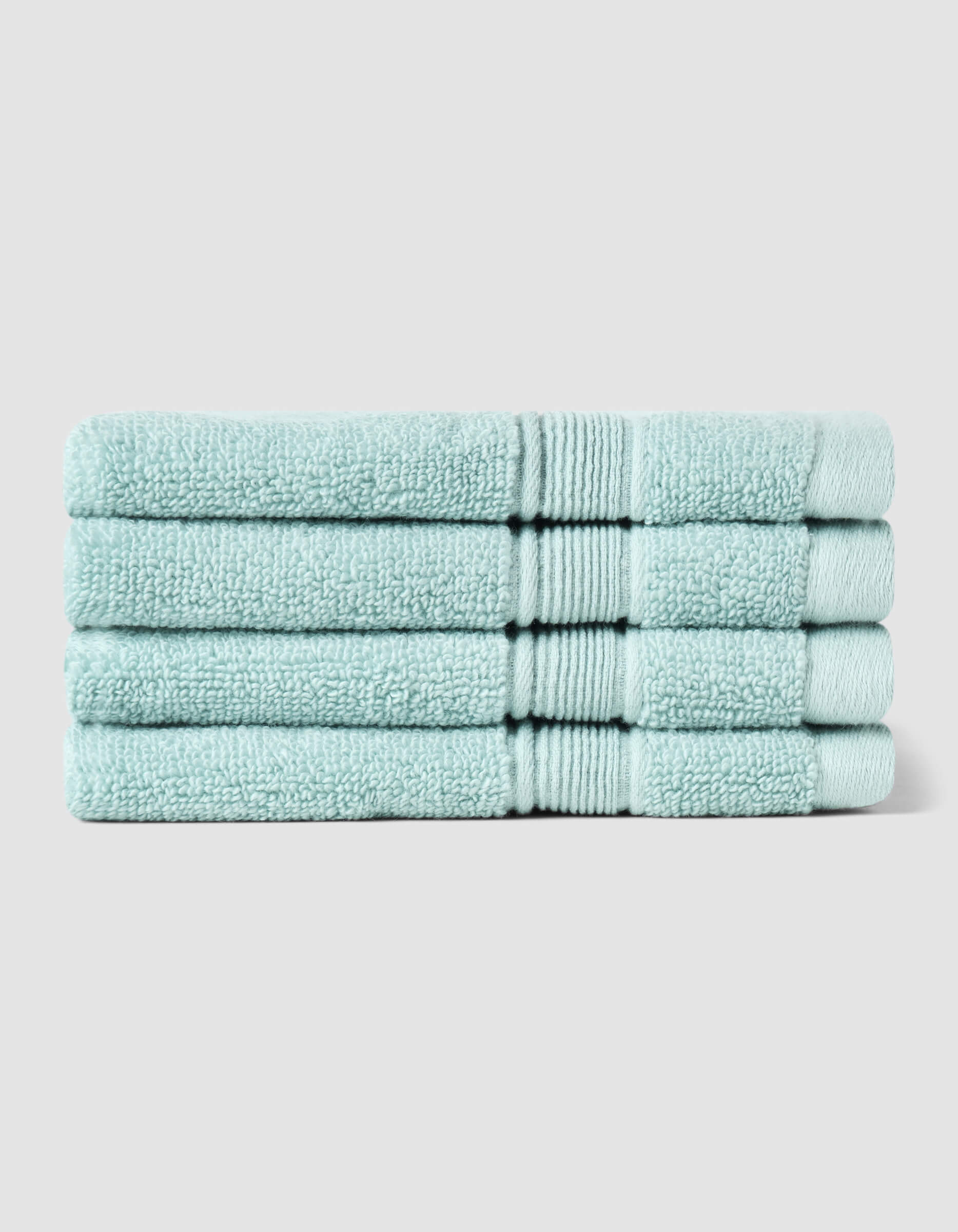 Four neatly folded Luxe Washcloths by Cozy Earth, in light blue, stacked on top of each other against a plain light gray background.|Color:Tide