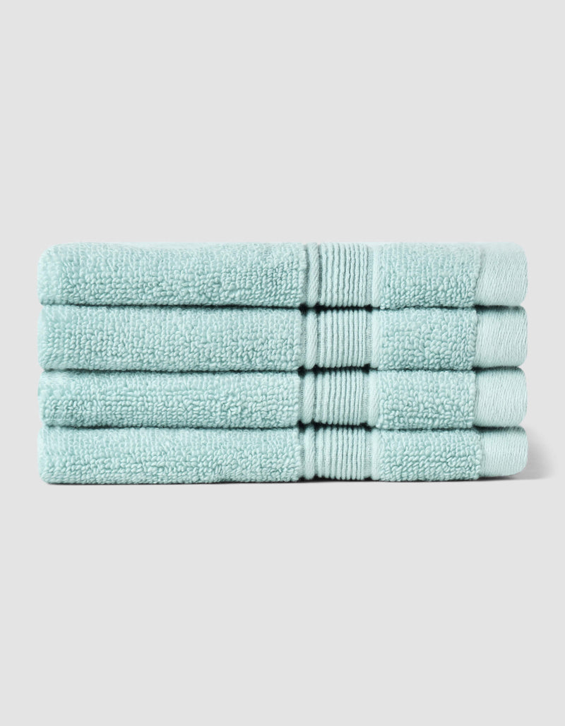 Four neatly folded Luxe Washcloths by Cozy Earth, in light blue, stacked on top of each other against a plain light gray background.