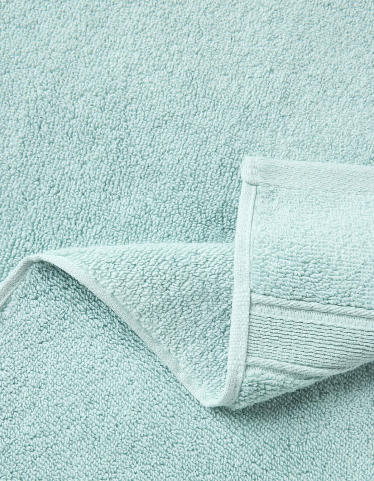 A close-up of Cozy Earth Luxe Washcloths in light blue, with one corner neatly folded to display the plush terry texture and detailed stitched edging.|Color:Tide