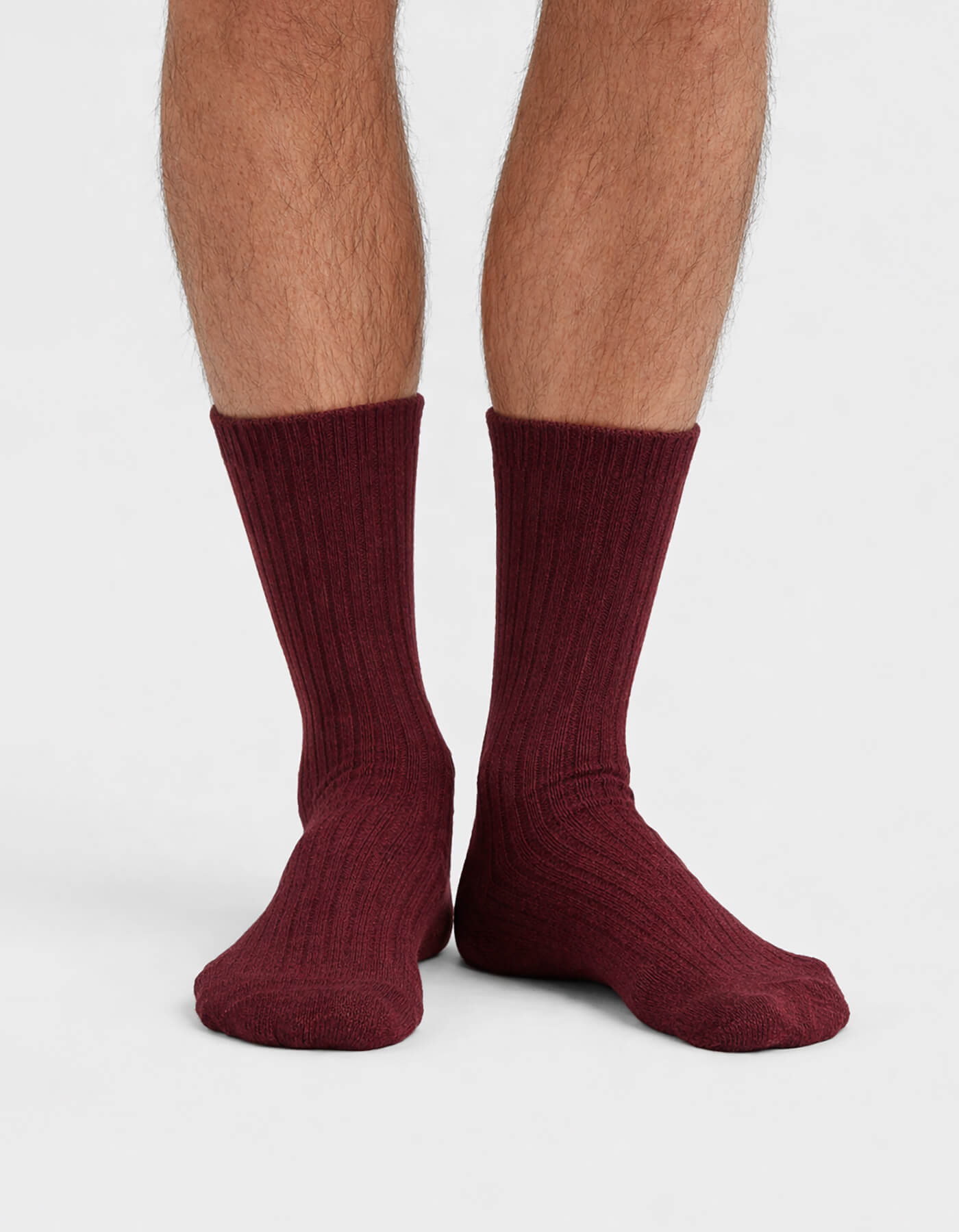 A close-up of a person's lower legs and feet wearing Cozy Earth’s The Plush Lounge Calf Sock 3-Pack in burgundy, ribbed, quarter-length style, set against a plain white background.