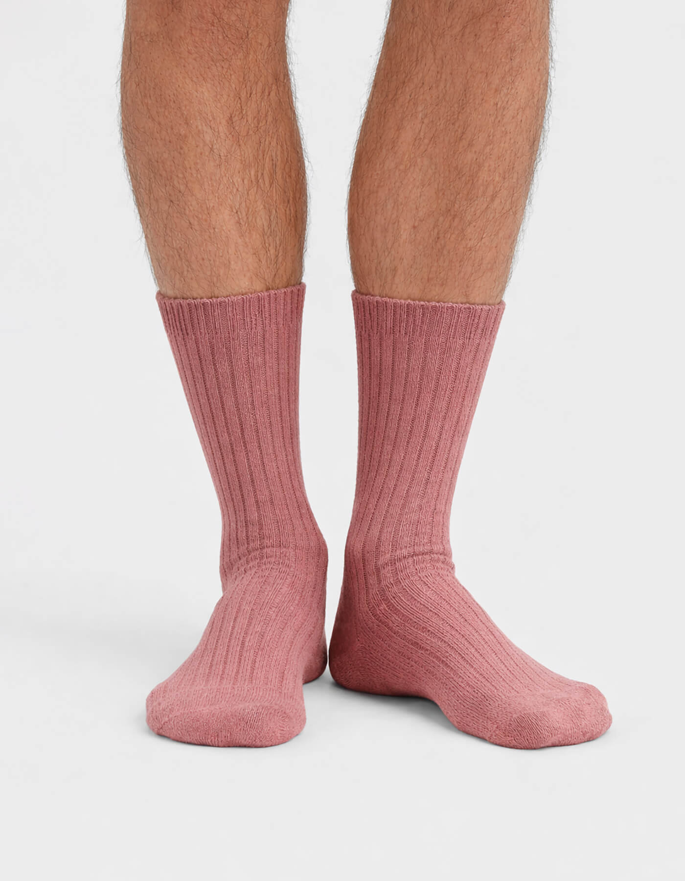 A close-up of a person's lower legs and feet wearing Cozy Earth’s The Plush Lounge Calf Sock 3-Pack in pink, ribbed, calf-length style, set against a plain white background.