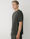 A person with short blonde hair stands in profile against a plain white background, wearing the Cozy Earth Men's Brushed Bamboo Raglan Tee - Last Chance in dark gray.