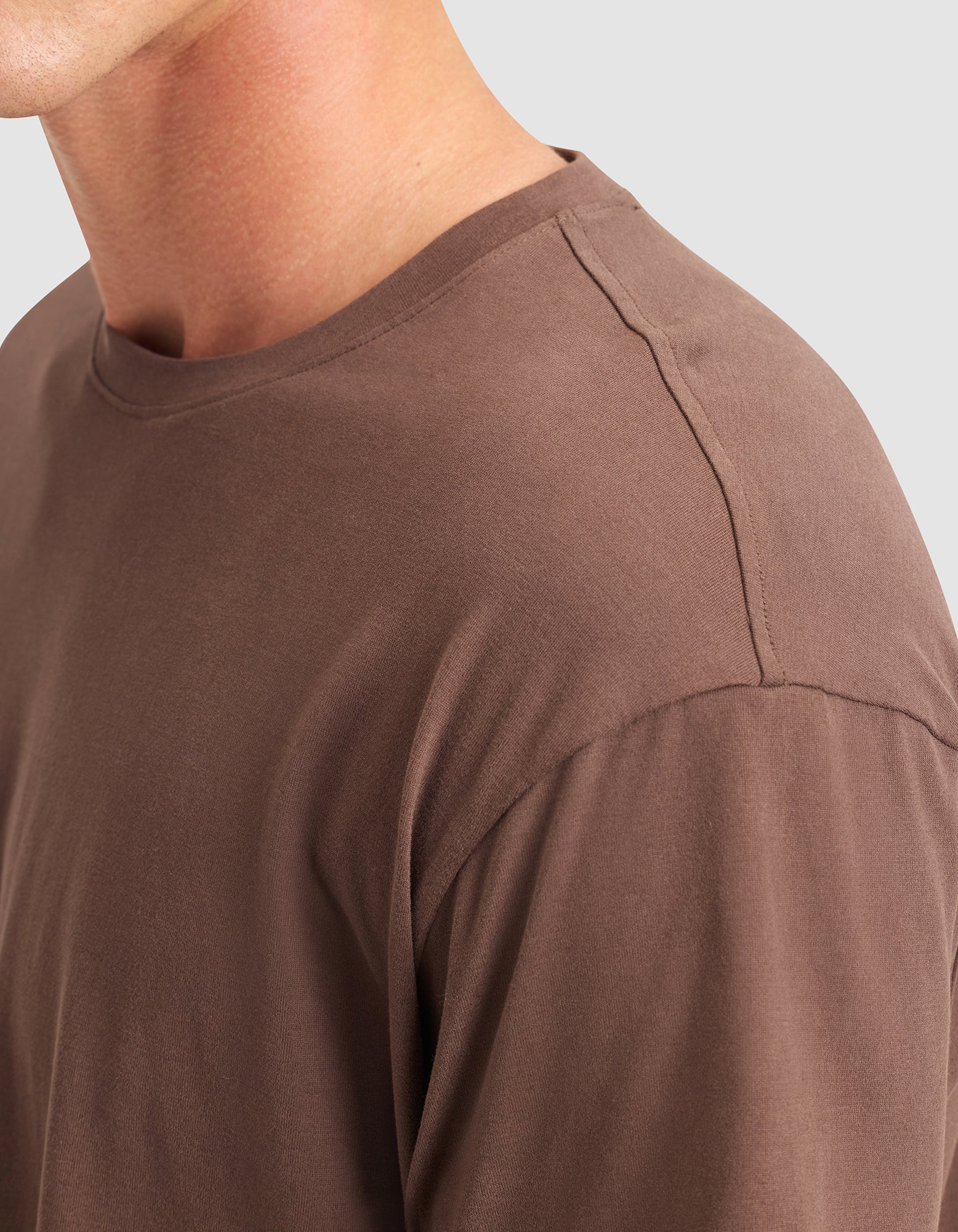 Close-up of a person wearing the Cozy Earth Men's All Day Tee in brown, highlighting the crew neckline, shoulder, and upper chest against a light gray background. 