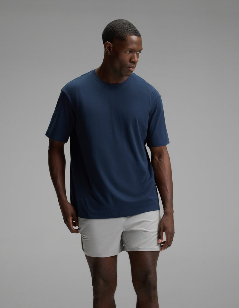 A man wearing the Cozy Earth Men’s All Day Tee in Eclipse stands against a plain gray background, looking to his left with a neutral expression.