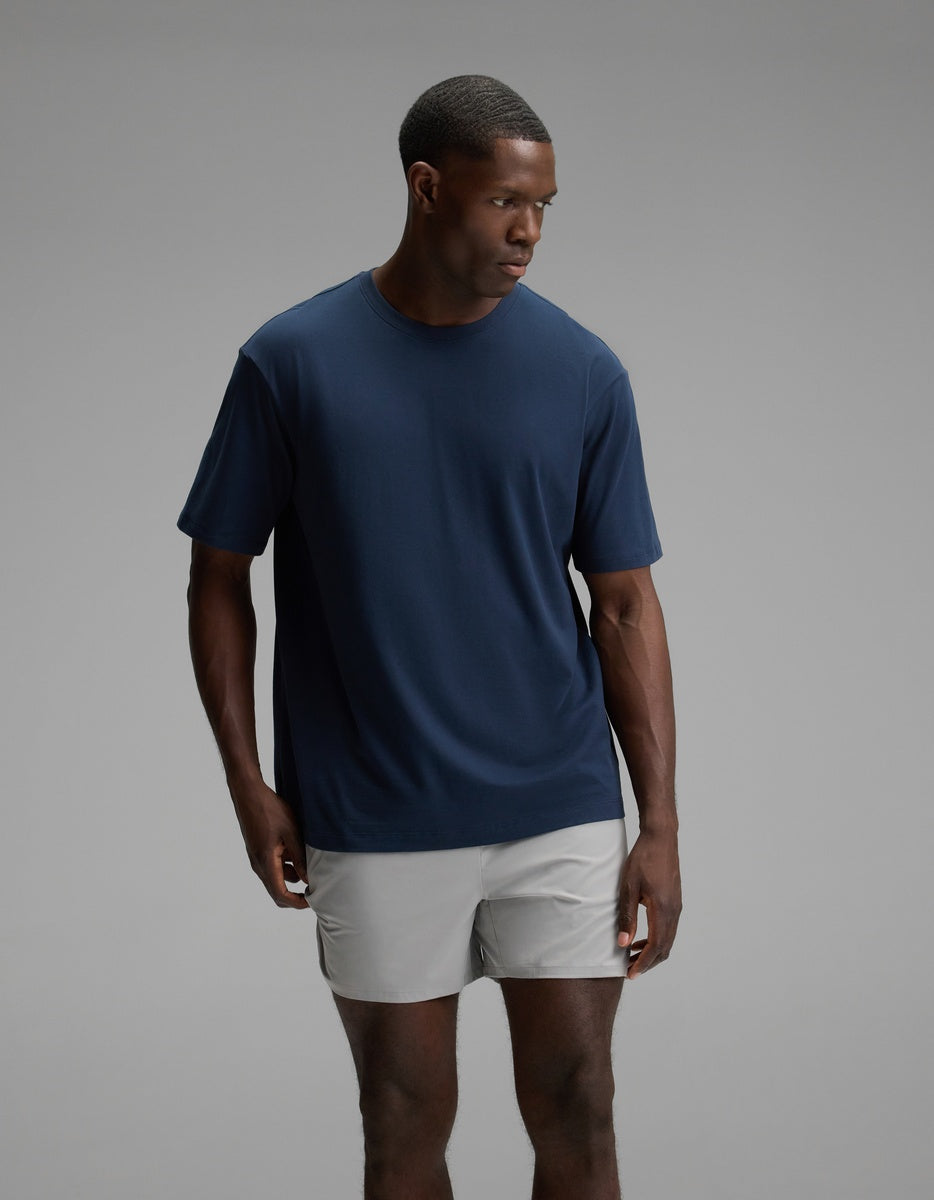 A man wearing the Cozy Earth Men’s All Day Tee in Eclipse stands against a plain gray background, looking to his left with a neutral expression.|Color:Eclipse