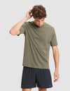 A man with curly brown hair wears the Cozy Earth Men's All Day Tee in olive green and black shorts, standing against a plain light gray background, looking down and touching the back of his head. |Color:Olive