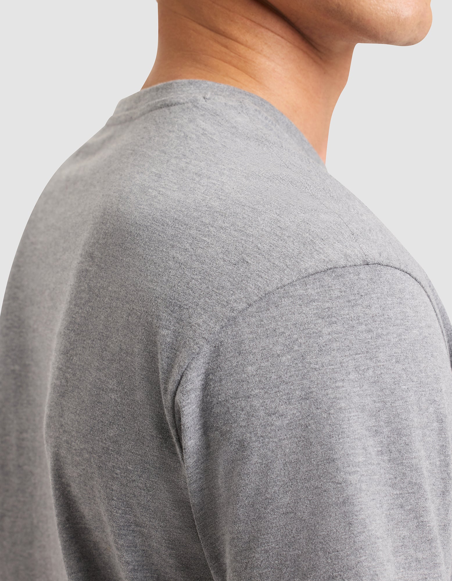 Close-up side view of a person wearing the Cozy Earth Men's All Day Tee in light grey, highlighting the shoulder, sleeve, and neckline details against a plain light background with the face mostly out of frame. 
