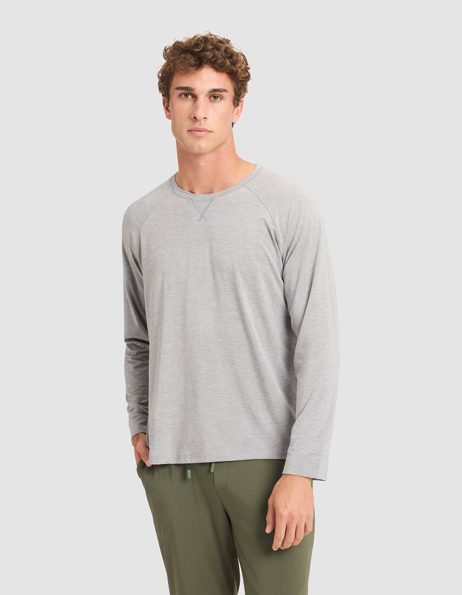 A man with curly brown hair wears the Cozy Earth Men's Bamboo Stretch-Knit Long Sleeve in light gray and olive green pants, standing against a plain light gray background. 