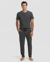 A man stands barefoot against a plain light background, wearing Cozy Earth’s Men's Bamboo Stretch-Knit Lounge Tee & Pant Pajama Set in Charcoal.|Color:Charcoal