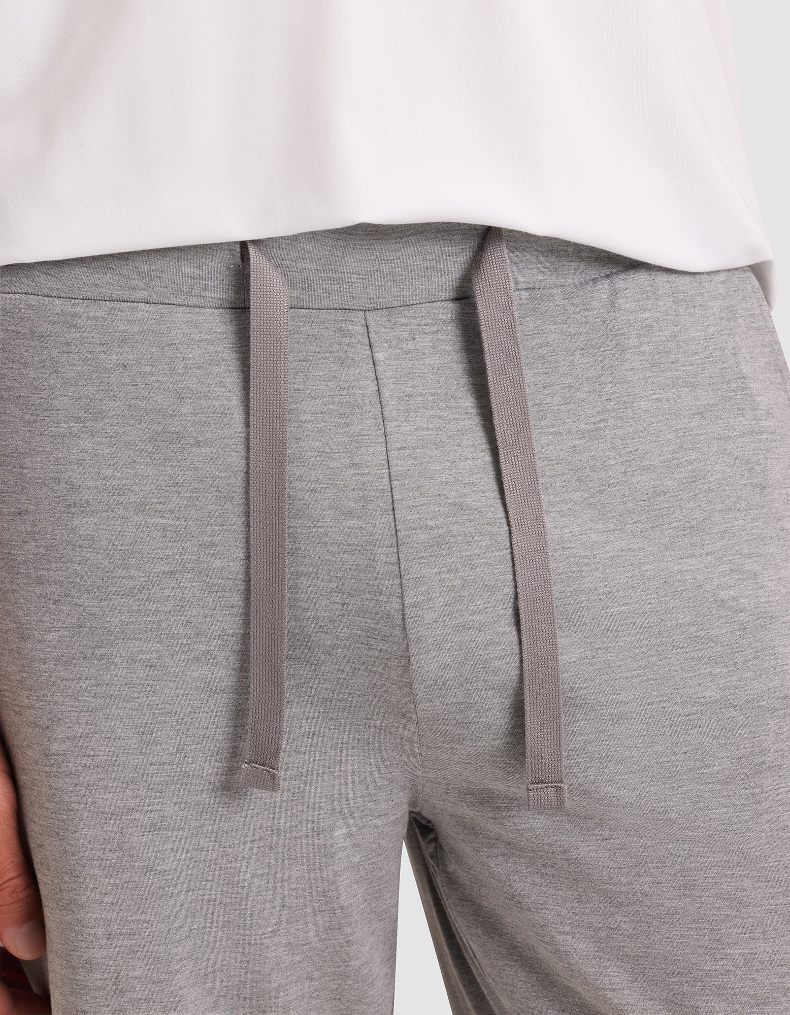 Close-up of a person wearing Cozy Earth Men's Bamboo Stretch-Knit Pajama Shorts in light gray with a drawstring waist, paired with a partially visible white shirt. 