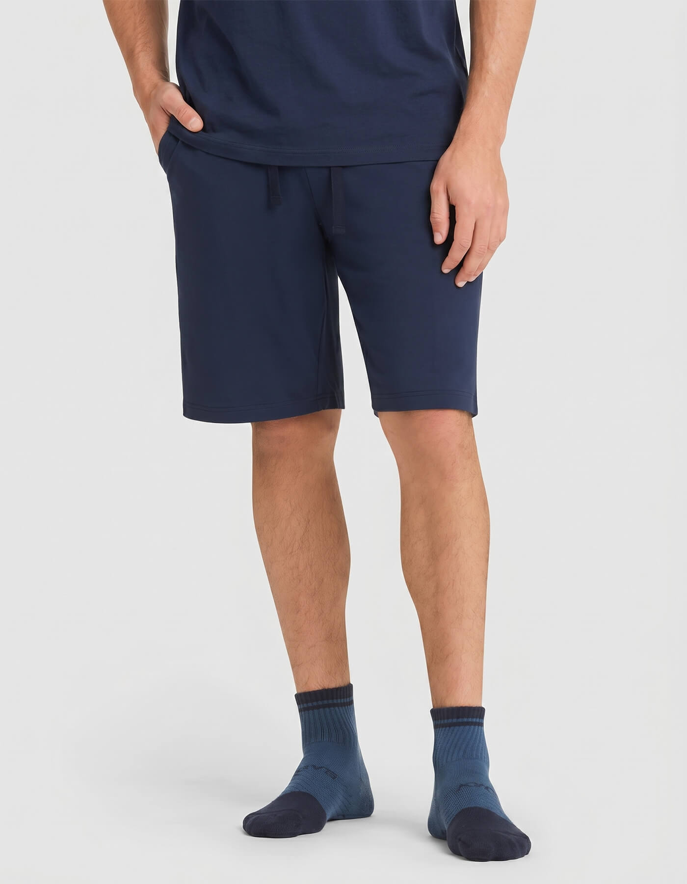 A person wearing Cozy Earth's Men's Bamboo Stretch-Knit Short Sleeve Pajama Set in navy stands against a plain light background, with only the lower half of the body visible.