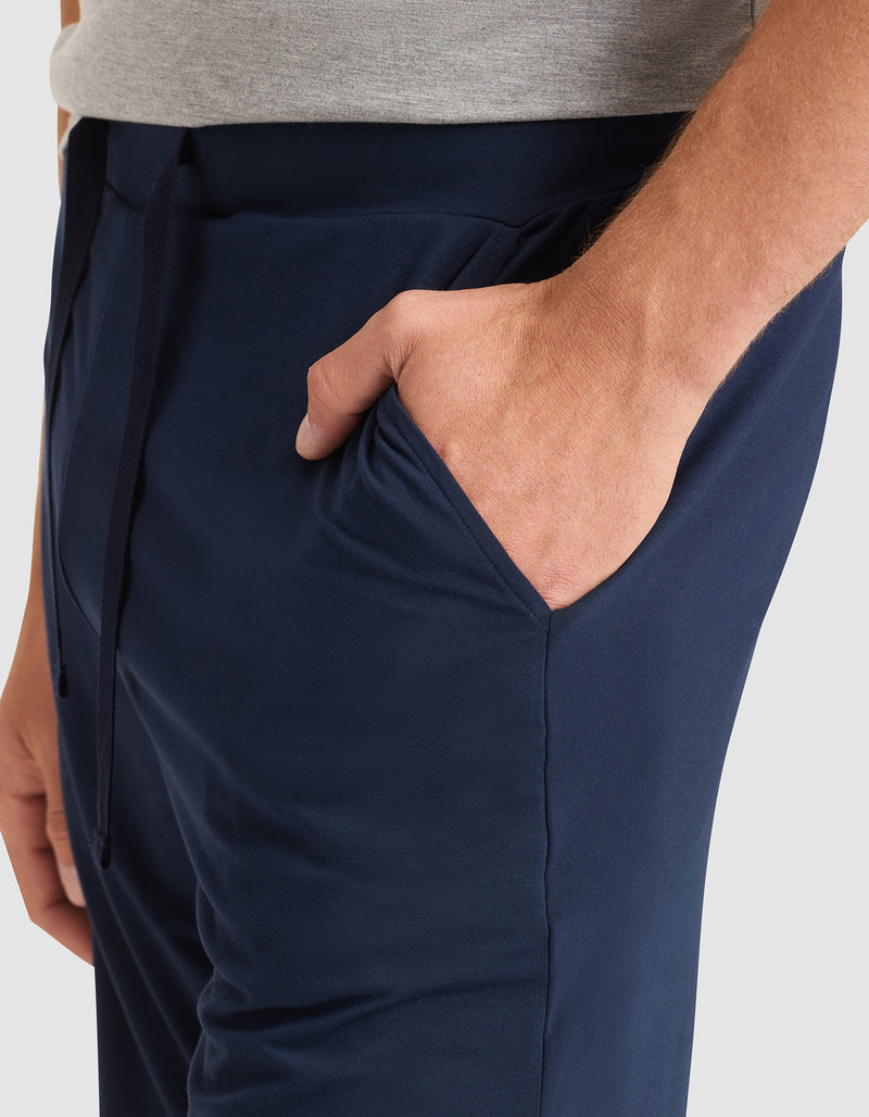 A person wearing Cozy Earth Men's Bamboo Stretch-Knit Pajama Shorts in navy blue and a light gray shirt stands with their right hand in the shorts pocket.