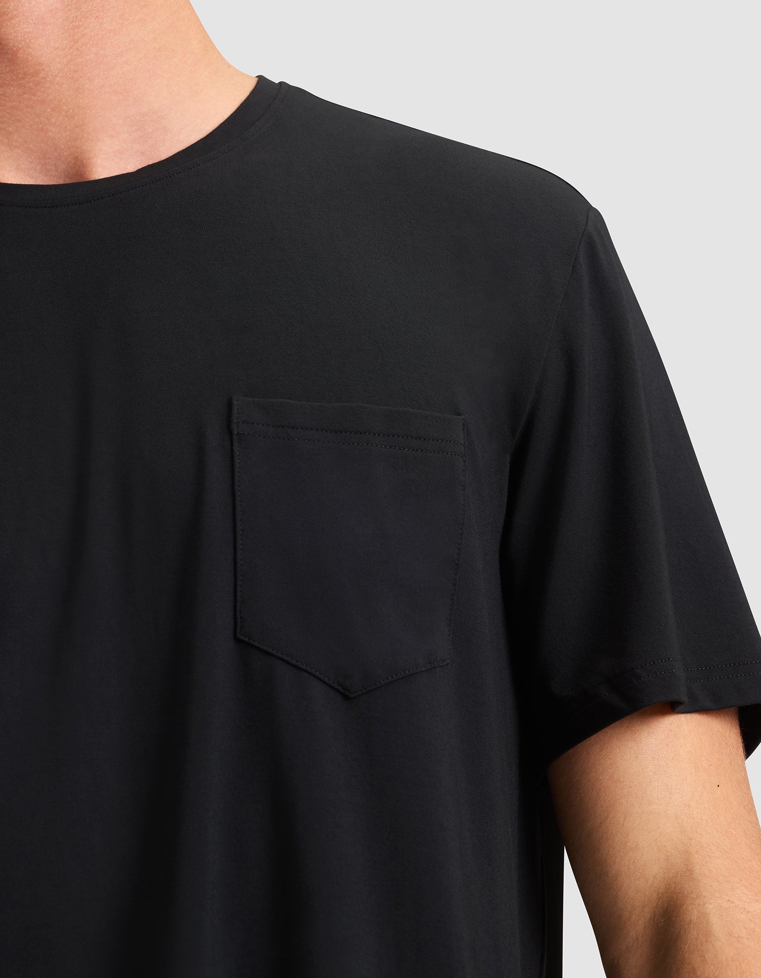Close-up of a person wearing the Cozy Earth Men's Bamboo Stretch-Knit Lounge Tee in black, featuring a chest pocket and short sleeves, shown from shoulders to mid-arm against a light gray background. 