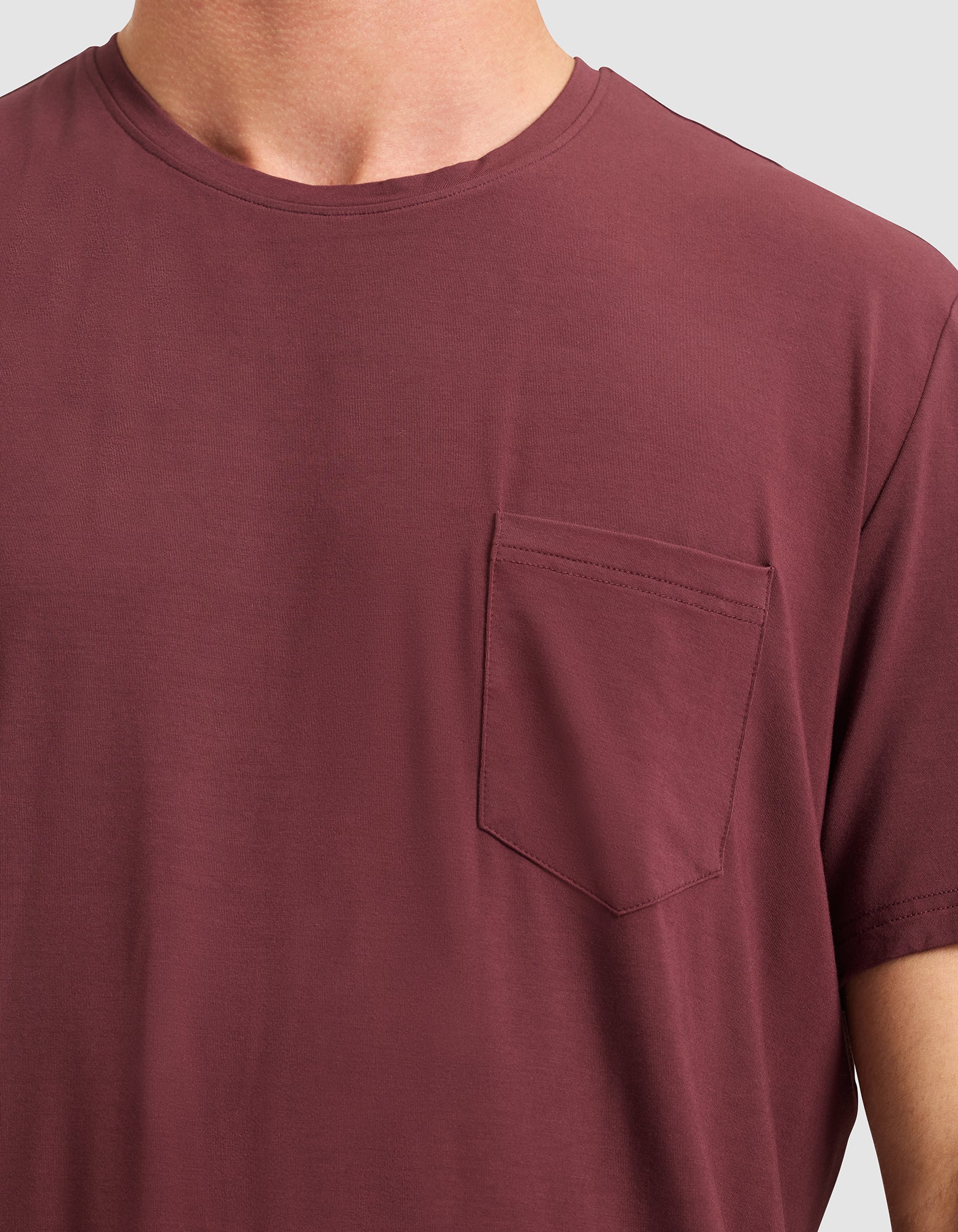 Close-up of a person wearing Cozy Earth's Men's Bamboo Stretch-Knit Lounge Tee in maroon, featuring a left chest pocket. Background is plain light gray.