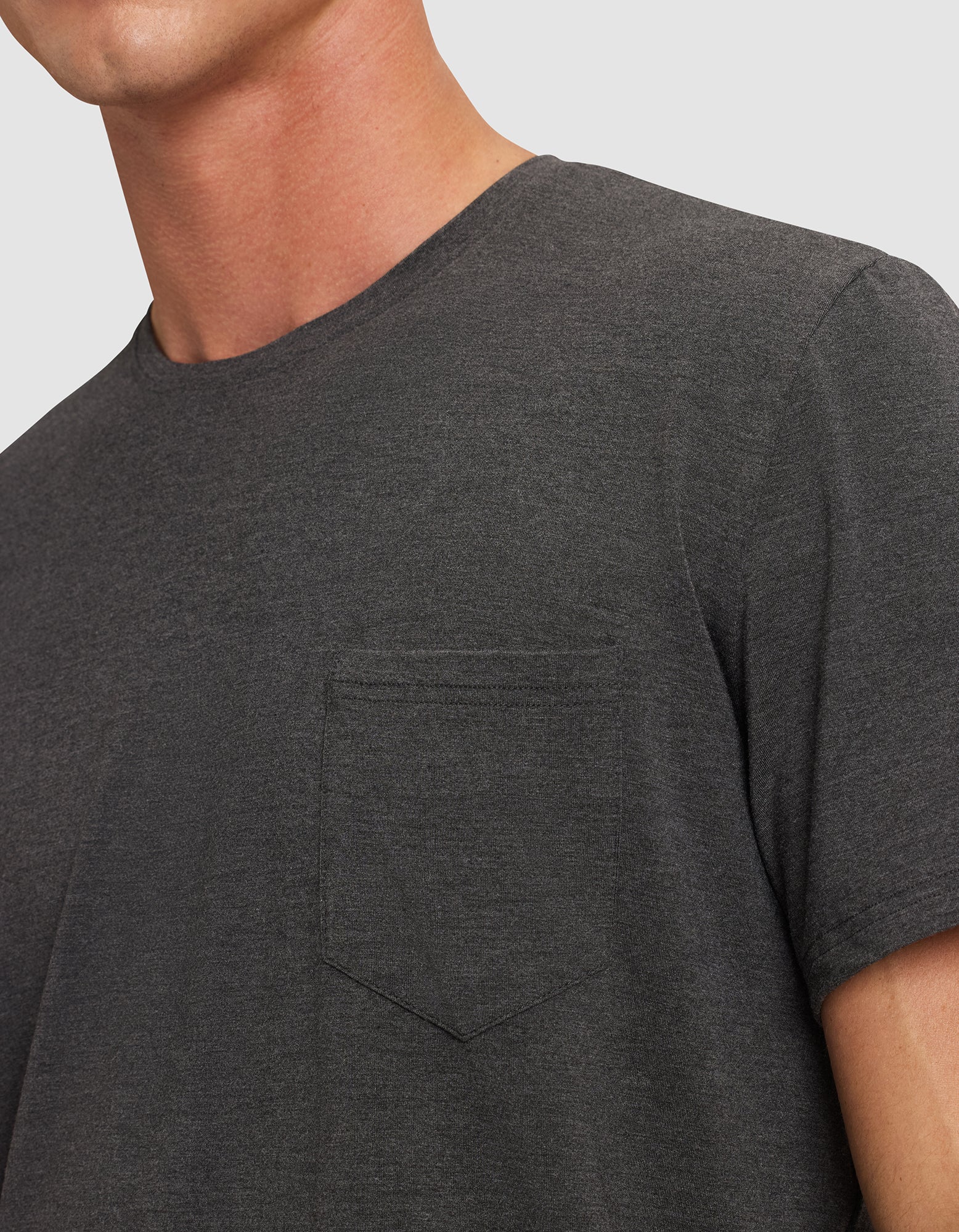 A close-up of a person wearing the Cozy Earth Men's Bamboo Stretch-Knit Lounge Tee in dark gray, featuring a crew neck and small chest pocket, with part of their neck and upper chest visible against a plain background.
