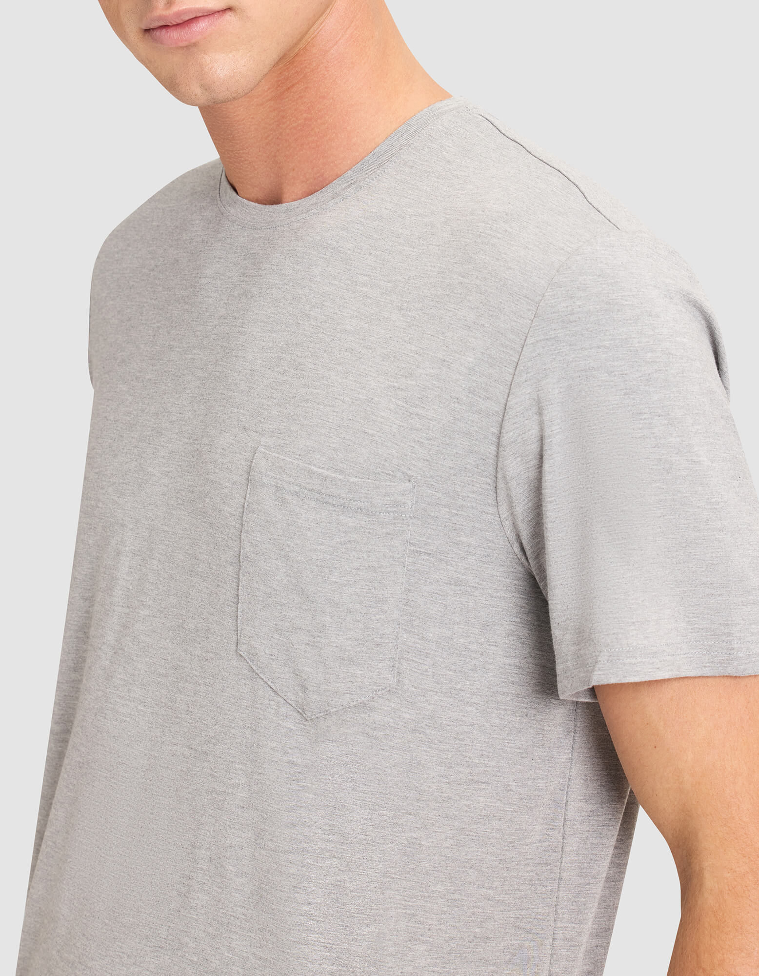 A person wears the Cozy Earth Men's Bamboo Stretch-Knit Lounge Tee in light gray with a chest pocket, shown from shoulders to mid-torso against a plain light background. The person's face is partially visible. 