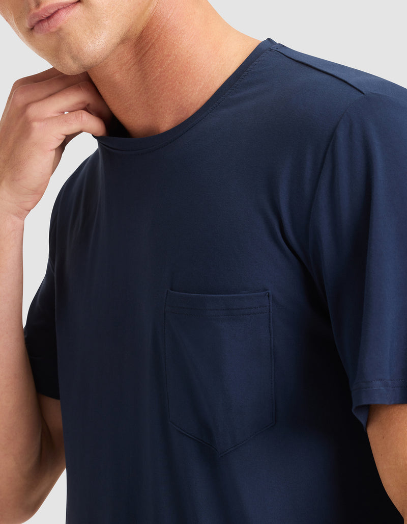 A person wearing the Cozy Earth Men's Bamboo Stretch-Knit Lounge Tee in navy blue, with a chest pocket, touches their neck. The image shows only the upper torso and part of the face.