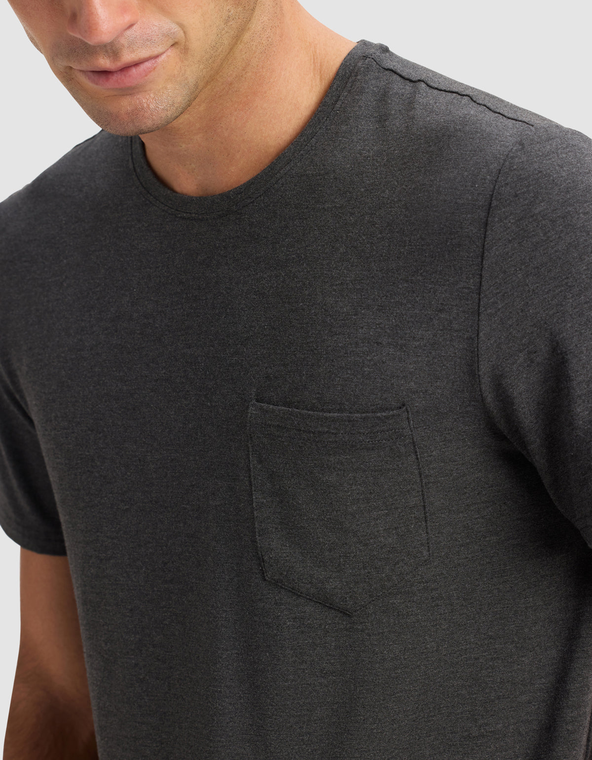 A man wears the Cozy Earth Men's Bamboo Stretch-Knit Lounge Tee in charcoal gray with a chest pocket, shown from shoulders to mid-torso against a light gray background. His face is partially visible.|Color:Charcoal