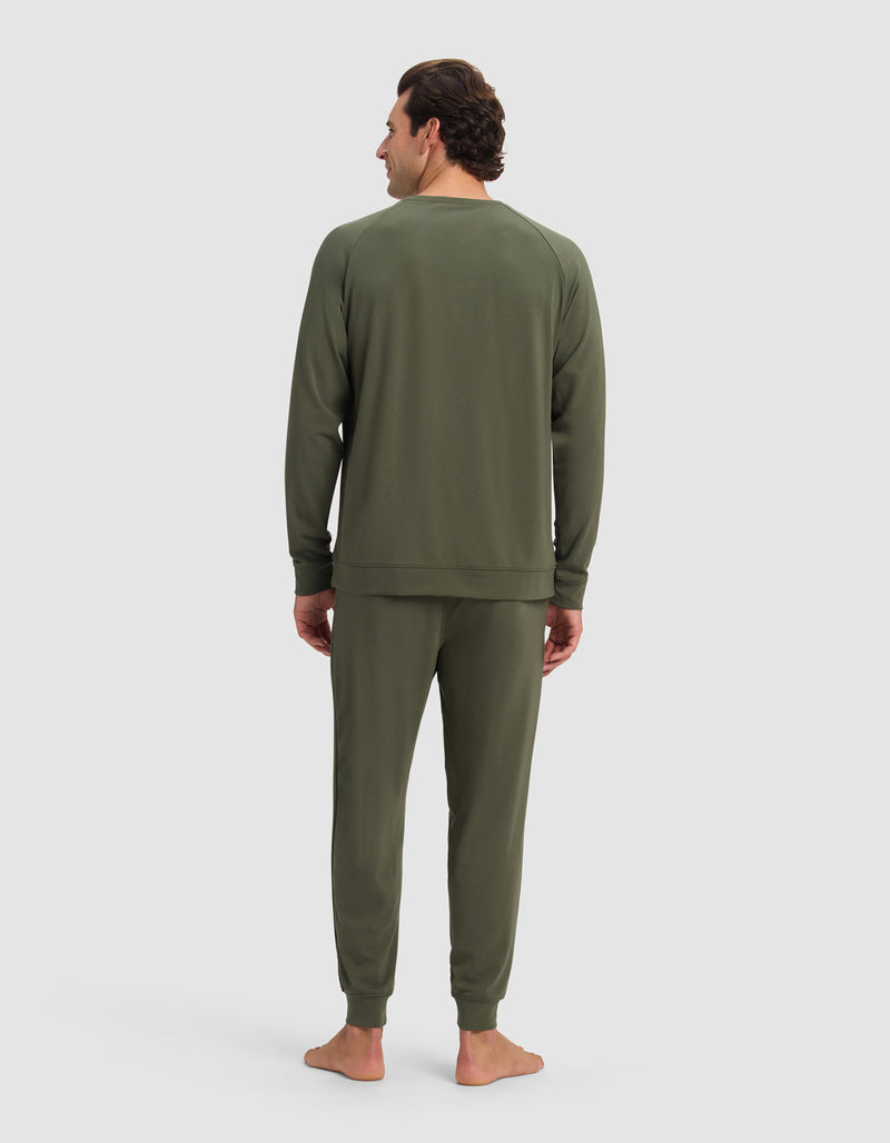 A man stands barefoot facing away, wearing the Cozy Earth Men's Brushed Bamboo Jogger Set in olive green against a plain light background.