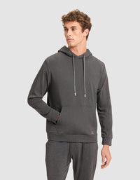 A young man models the Cozy Earth Men's Brushed Bamboo Hoodie in dark gray with drawstrings, paired with matching sweatpants, standing with one hand in his pocket against a plain light gray background.